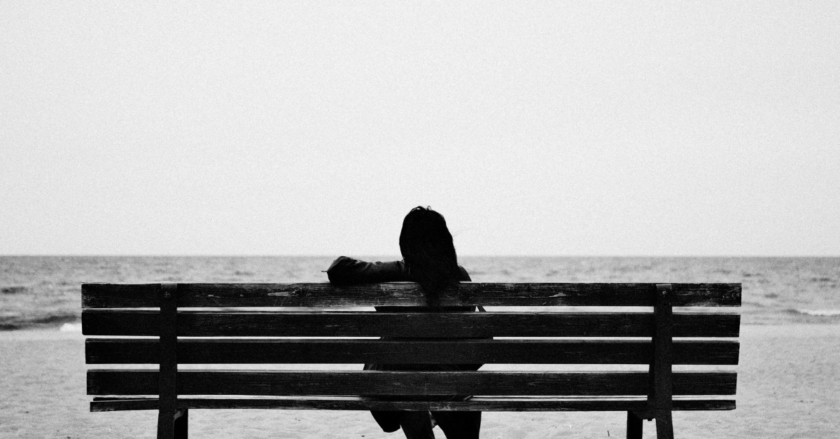 Woman sitting alone on a bench by the sea. Symbolic of quiet reflexion and emotional support after miscarriage.
